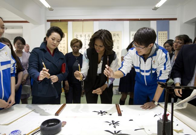 Peng Liyuan, wife of Chinese President Xi Jinping, left, shows first lady Michelle Obama how to hold a writing brush as they visit a Chinese traditional calligraphy class in Beijing on Friday, March 21. The first lady is on <a href="index.php?page=&url=http%3A%2F%2Fwww.cnn.com%2F2014%2F03%2F21%2Fpolitics%2Fgallery%2Fmichelle-obama-china%2Findex.html">an official visit</a> to expand relations between the United States and China. Click through the gallery to see her other international travels through the years.