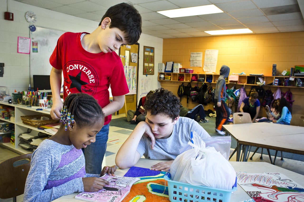 Max Bradley, 13, right, helps Carrington Stallworth, 7, with her reading while Ian Ferreira, 11, looks on. At Hess Academy, it's common to see some students working at desks while others are sprawled on the floor.