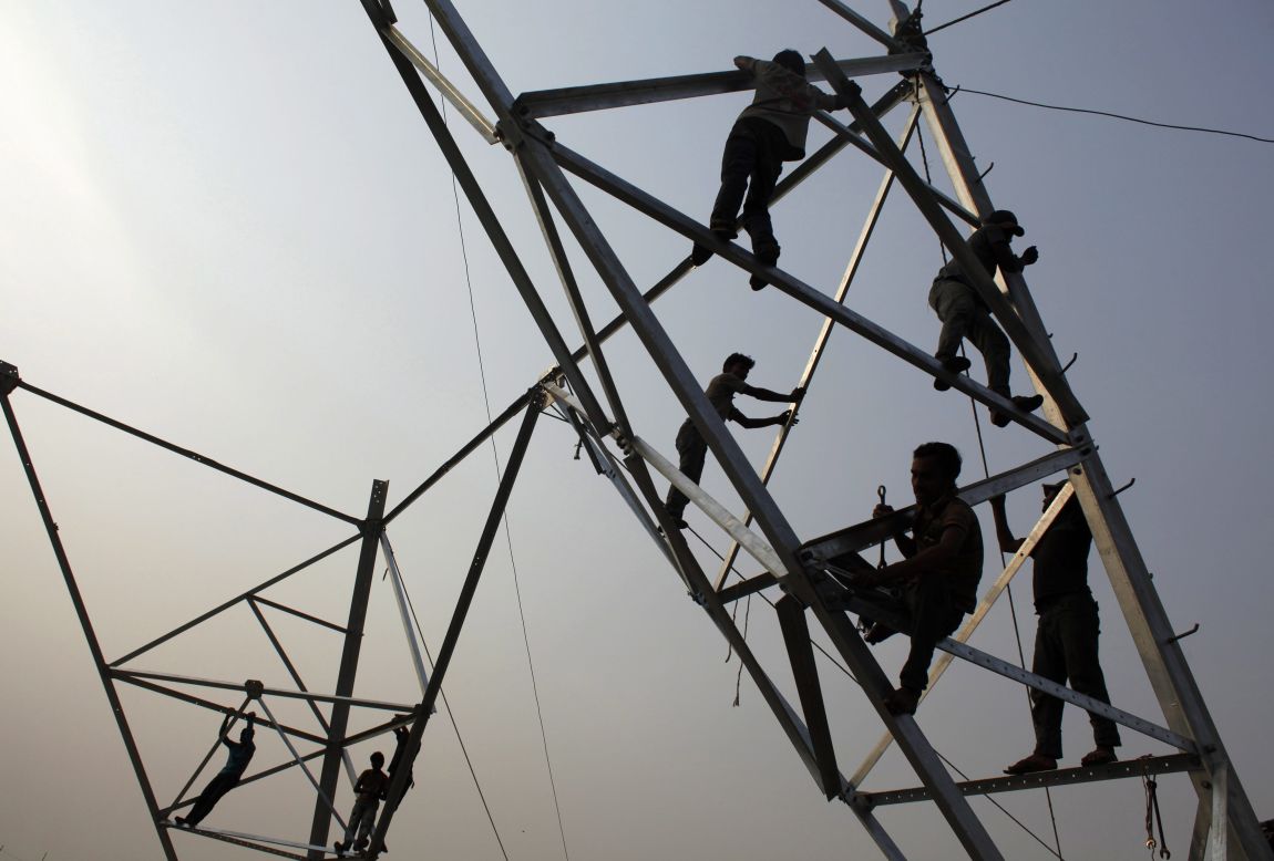 Laborers work without safety equipment as they install electricity poles in Dhaka, Bangladesh, on Friday, March 21.