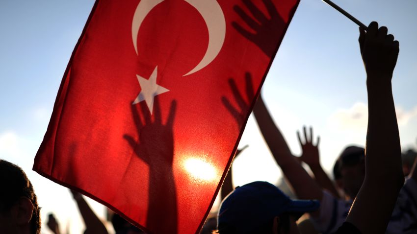 A protester holds up a Turkish flag as others raise their hands during a demonstration in Taksim square in Istanbul on June 8, 2013. Thousands of angry Turks took to the streets on June 8 to join mass anti-government protests, defying Prime Minister Recep Tayyip Erdogan's call to end the worst civil unrest of his decade-long rule. Erdogan, meanwhile, was meeting in Istanbul with top officials of his Justice and Development Party (AKP) to discuss the crisis, and a deputy prime minister was due to make a speech later on June 8. AFP PHOTO/BULENT KILIC (Photo credit should read BULENT KILIC/AFP/Getty Images)