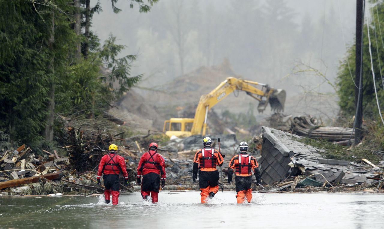 Search-and-rescue workers wade through water covering a highway near Darrington on Thursday, March 27. The landslide left buildings covered in up to 40 feet of mud.