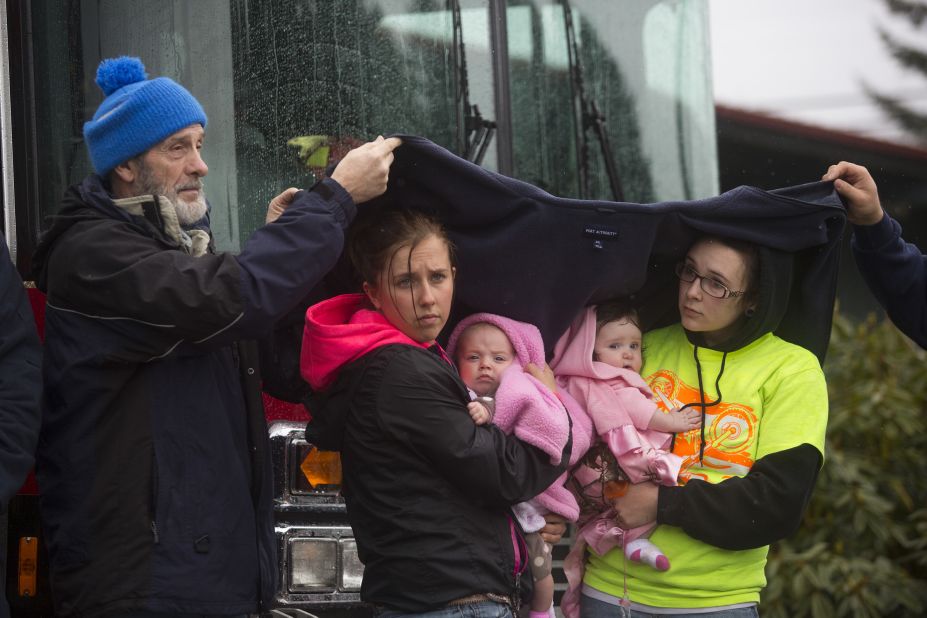 Ralph Jones helps provide shelter for Brooke Odenius, right, Klarissa Calviste and their baby daughters during the moment of silence at the fire house in Darrington.