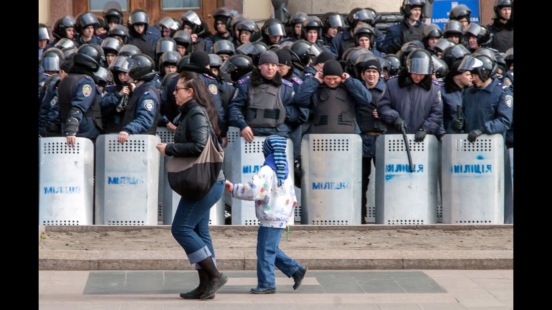 A woman and child walk past a line of police officers during a rally in Kharkiv on March 30.