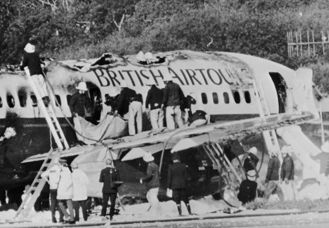 Firemen examining the wreckage of a British Airtours 747 that burst into flames at Manchester Airport.