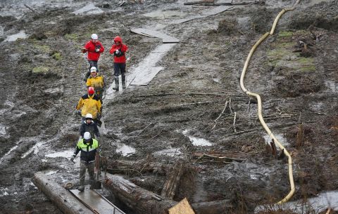 Search-and-rescue teams use a path of plywood to walk through a muddy field in Arlington, Washington, on March 30.