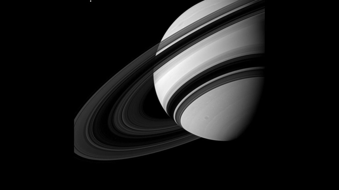 Tetis, arriba a la izquierda, se ve pequeña en comparación a Saturno mientras orbita el planeta, aunque los científicos creen que la luna es mucho más grande que el sistema de anillos de Saturno.
