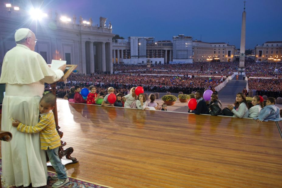 A young boy hugs Francis as he delivers a speech in St. Peter's Square in October 2013. The boy, part of a group of children sitting around the stage, played around the Pope as the Pope continued his speech and occasionally patted the boy's head.  