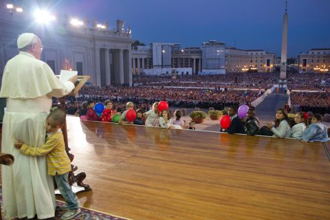 A young boy hugs Francis as he delivers a speech in St. Peter's Square in October 2013. The boy, part of a group of children sitting around the stage, played around the Pope as the Pope continued his speech and occasionally patted the boy's head.  