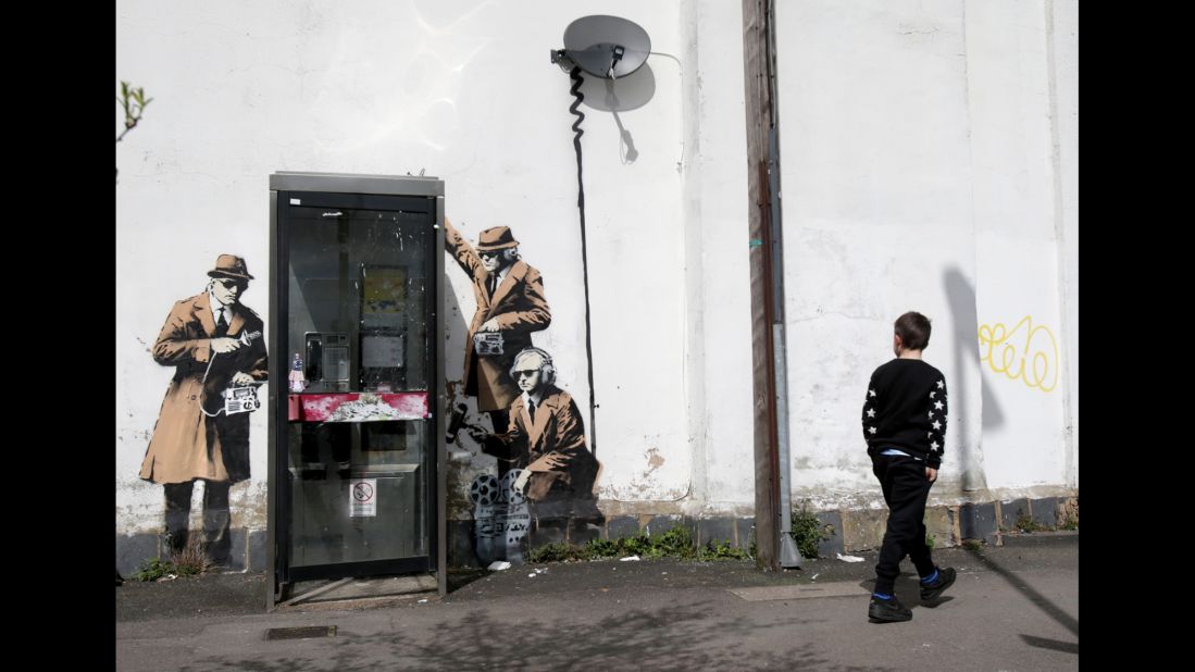 A boy walks past graffiti street art believed to be by Banksy in April 2014. The image depicts men in trench coats and dark glasses holding old-fashioned listening equipment -- apparently a commentary on government surveillance. The artwork appeared on the side of a house in Cheltenham near the Government Communications Headquarters, the UK equivalent of the National Security Agency. 