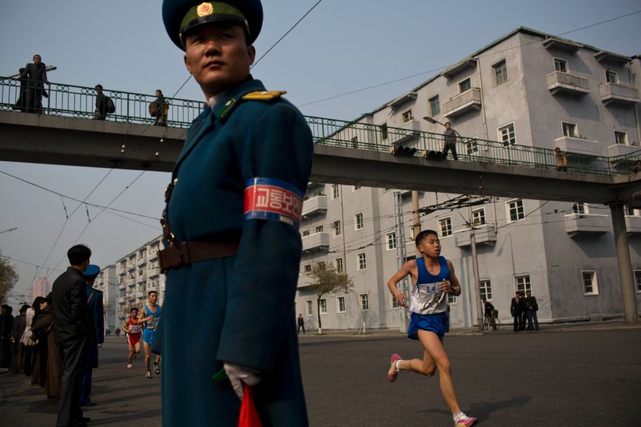 Runners pass under a pedestrian bridge in central Pyongyang as an official keeps watch.
