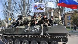 Men wearing military fatigues sit by a Russian flag and a white flag reading 'People's volunteer corps of Donetsk' as they ride on an armoured personnel carrier (APC) in the eastern Ukrainian city of Slavyansk on April 16, 2014.