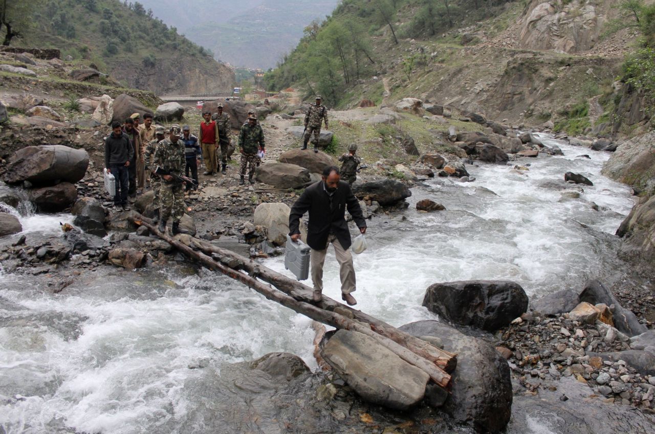An election official carries an electronic voting machine across a makeshift bridge after picking it up from a distribution center in Doda on April 16.