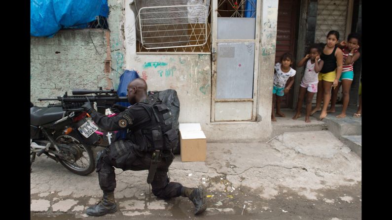 Girls watch a paramilitary police sniper secure an area in the favela as Brazilian soldiers conduct a search for weapons. The shantytown is just a few kilometers from Rio's international airport, where many of the expected 600,000 international fans will land.