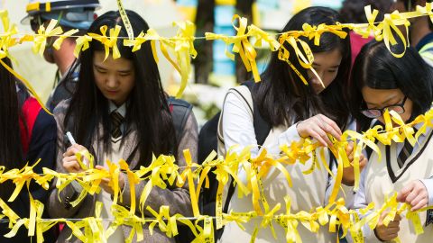 Schoolchildren tie yellow ribbons onto the roadside of a main gate at Danwon High School on April 24, 2014. 