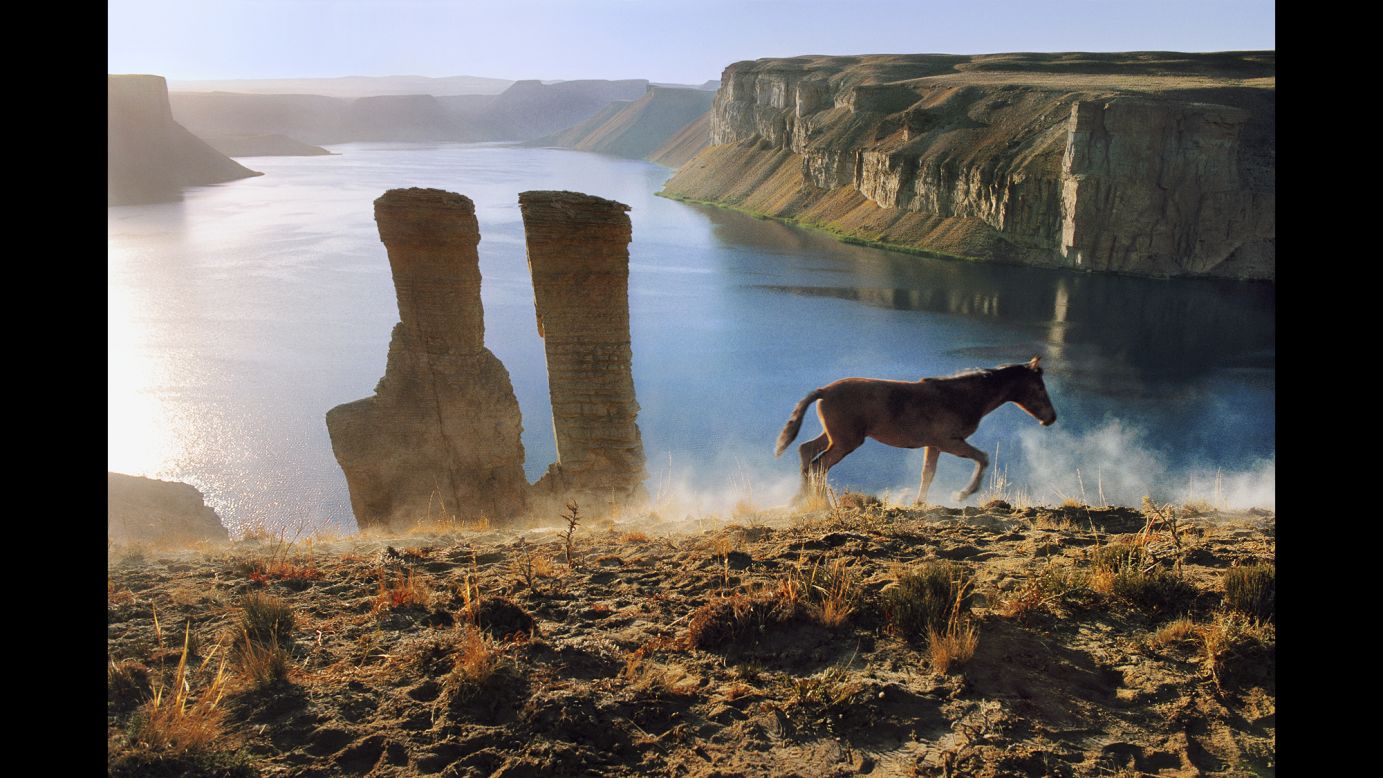 A colt runs after its mother past two vertical rock formations in Band-i-Amir, 2002.