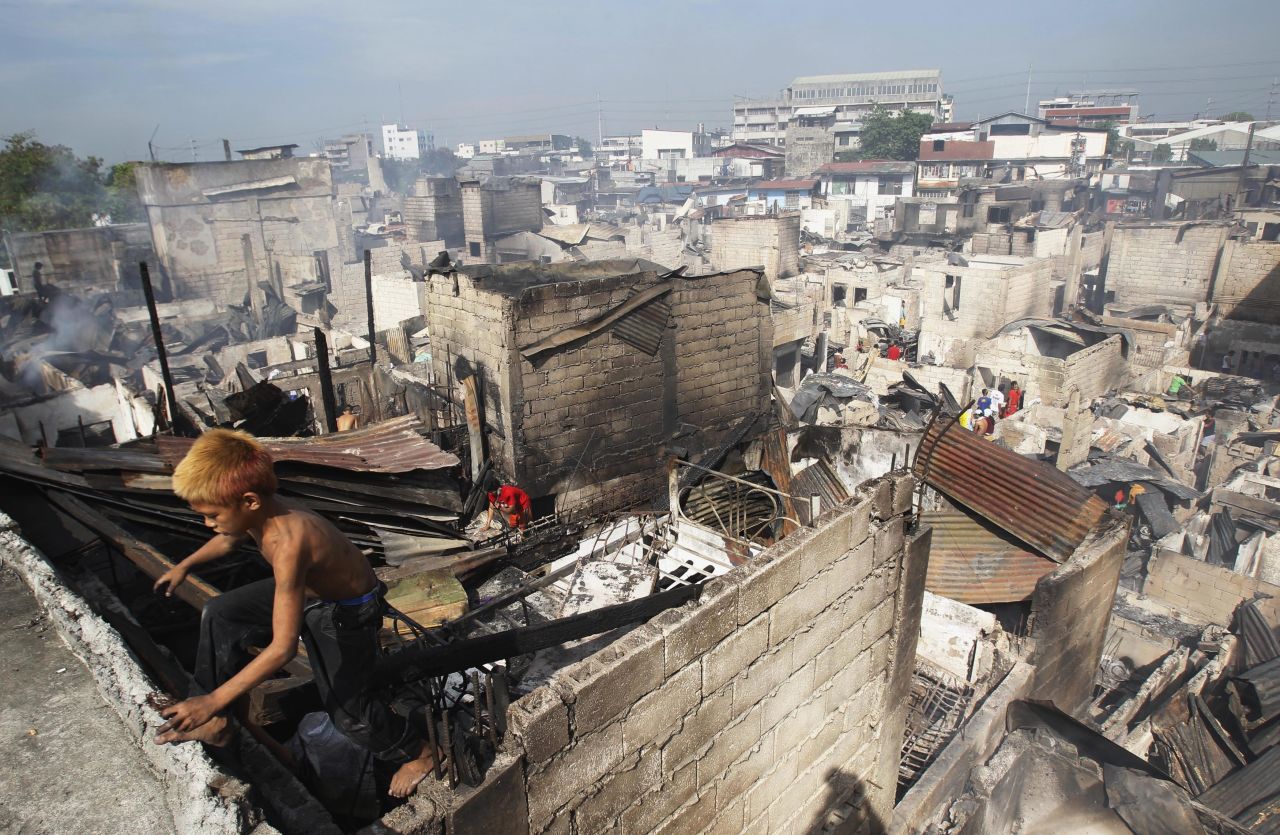 A boy climbs out of a charred shanty as he collects reusable materials after a fire razed a slum in Caloocan, Philippines, on Monday, April 21. 
