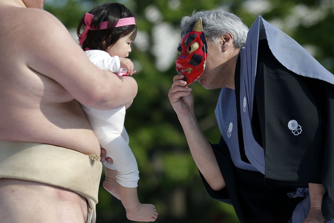 An inspector uses a mask of an <em>oni</em>, or demon, to try to make a baby cry. 