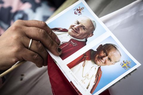 A card shows portraits of John XXIII, left, and John Paul II as pilgrims wait for the canonization ceremony to begin.
