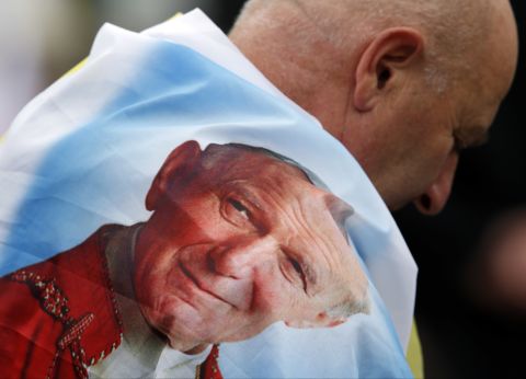 A man is wrapped in a flag bearing a picture of Pope John Paul II in St. Peter's Square.