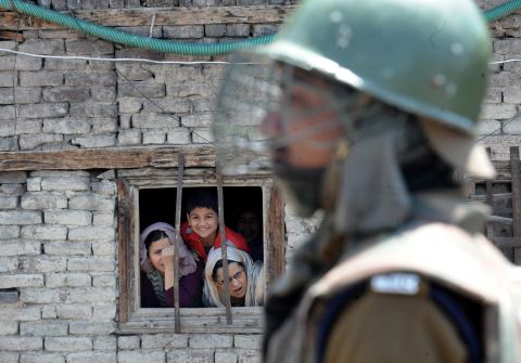 Kashmiri Muslims watch from a window as an Indian paramilitary soldier stands guard near the site of an explosion near the venue where an election campaign rally was to take place in downtown Srinagar on April 27.
