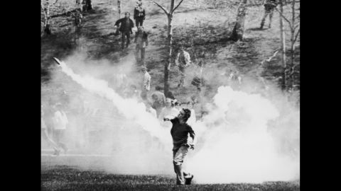 A student throws a tear gas canister back at National Guardsmen. After several standoffs, the troops headed back up a hill in the direction of the ROTC building. As they reached the top, they turned toward the demonstrators and opened fire.