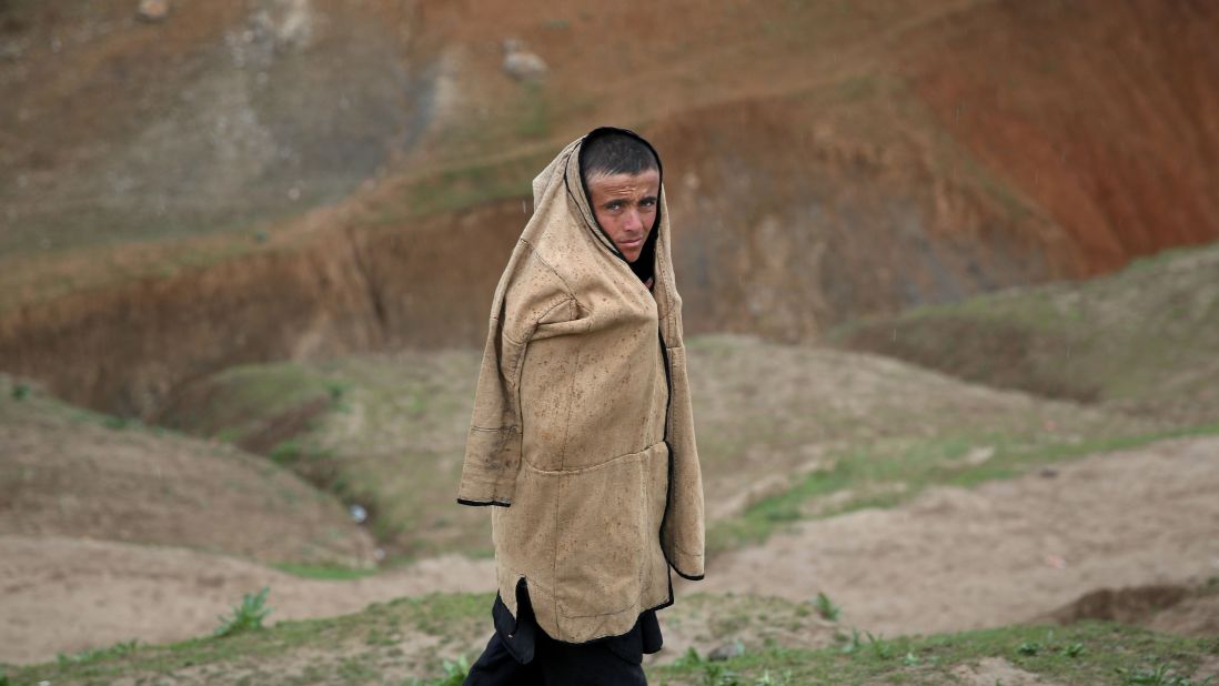 An Afghan teenager protects himself from the rain as he walks near the site of the landslide on May 4. 