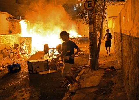 Residents run for cover during violent clashes between protesters and Brazilian Police Special Forces in a favela near Copacabana in Rio on April 22, 2014. Violent protests broke out in the city's landmark beachfront district following the death of a resident during clashes with the army in a nearby favela. 