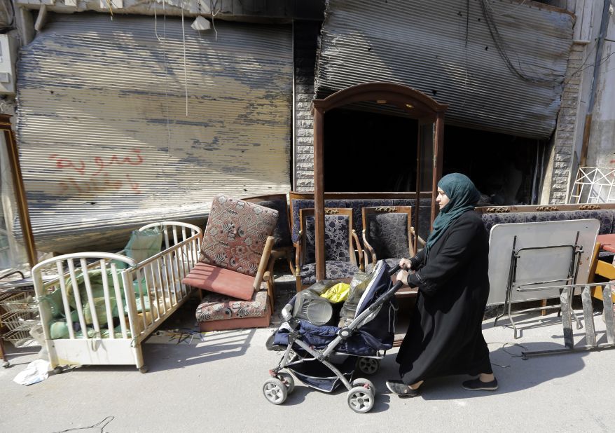 A Syrian woman pushes a baby stroller packed with belongings past furniture left on the side of the street in the Old City on May 12.