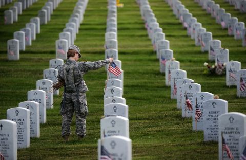 Staff Sgt. Kerrin Kampa, of the Old Guard Fife and Drum Corps, along with other soldiers, place flags in front of headstones at Arlington Cemetery.