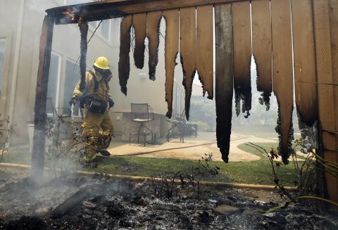 A firefighter puts water on a smoldering fence outside a home in Carlsbad on May 14.