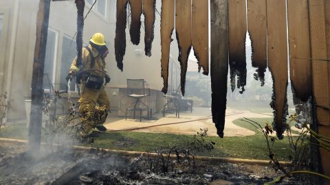 A firefighter puts water on a smoldering fence outside a home in Carlsbad on May 14.