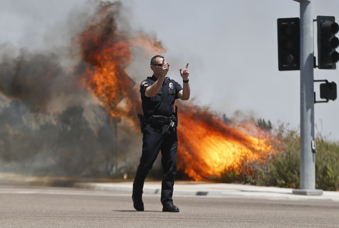 A Carlsbad police officer turns traffic away as flames rage behind him on May 14.