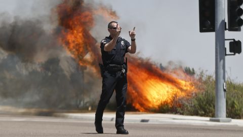 A Carlsbad police officer turns traffic away as flames rage behind him on May 14.
