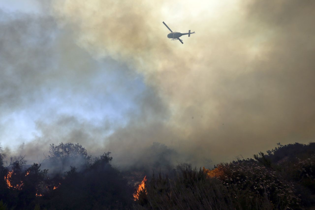 A helicopter flies over burning vegetation near homes in Carlsbad on May 14.
