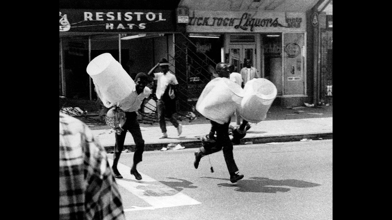 Two youths, carrying lampshades from a looted store, run down a street in the Watts neighborhood of Los Angeles on August 13, 1965. The Watts Riots were sparked by tensions between the city's black residents and police. The six days of violence left 34 dead and resulted in $40 million of property damage.