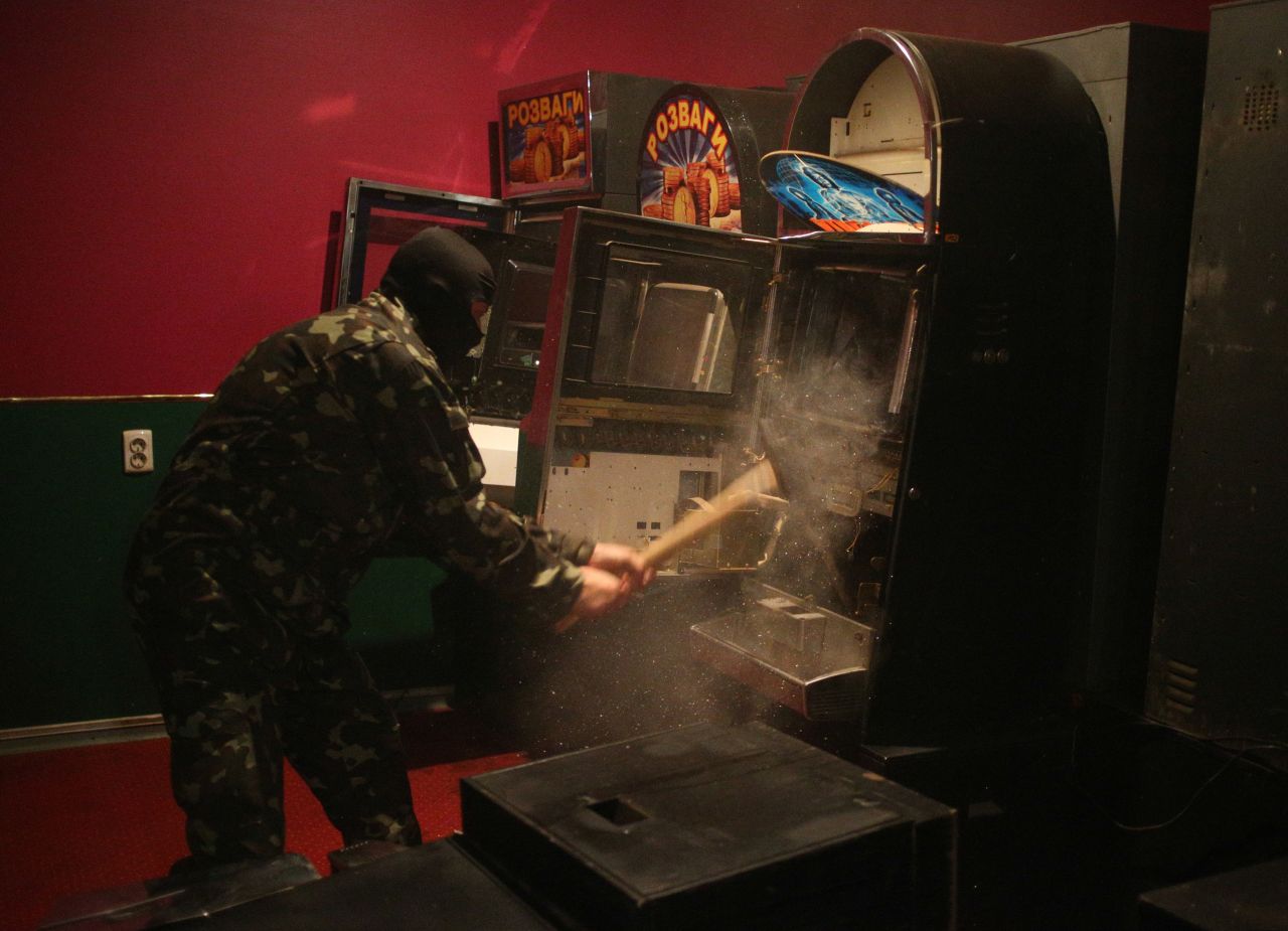 A member of a "self-defense" squad smashes a slot machine with a sledgehammer Monday, May 12, at an illegal club in Slovyansk.