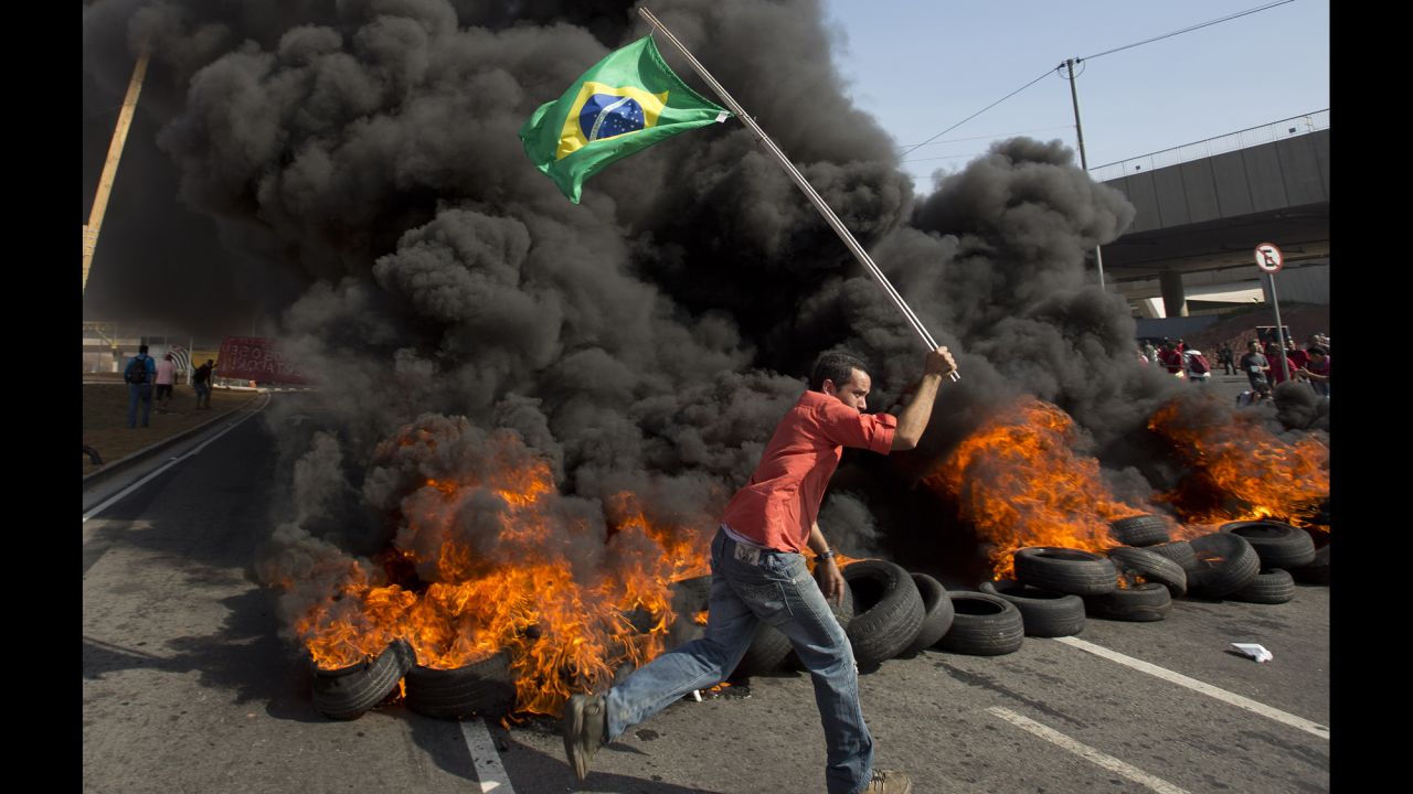 A member of the Homeless Workers Movement carries a Brazilian flag past burning tires near Itaquerao Stadium, which will be used during the World Cup in Sao Paulo.