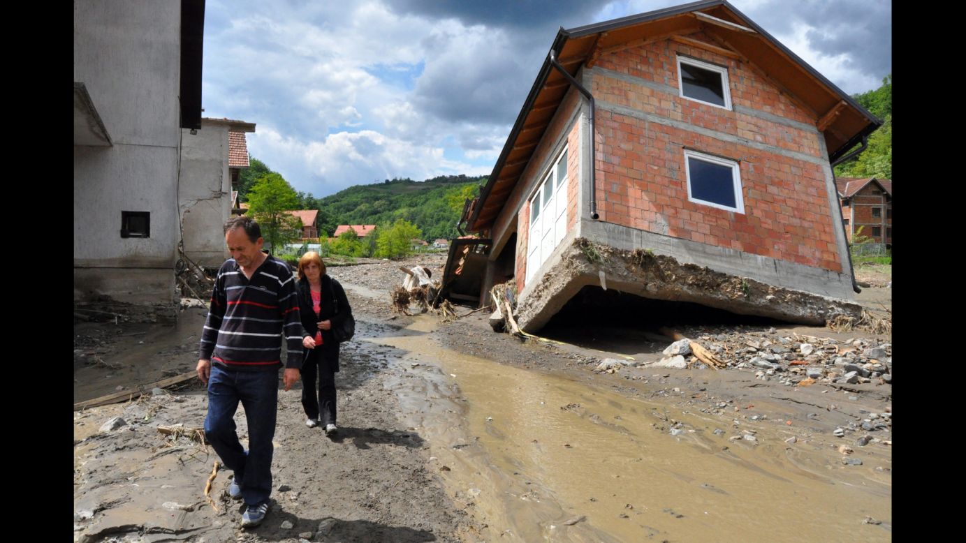 People walk past damaged houses in Krupanj on Sunday, May 18.