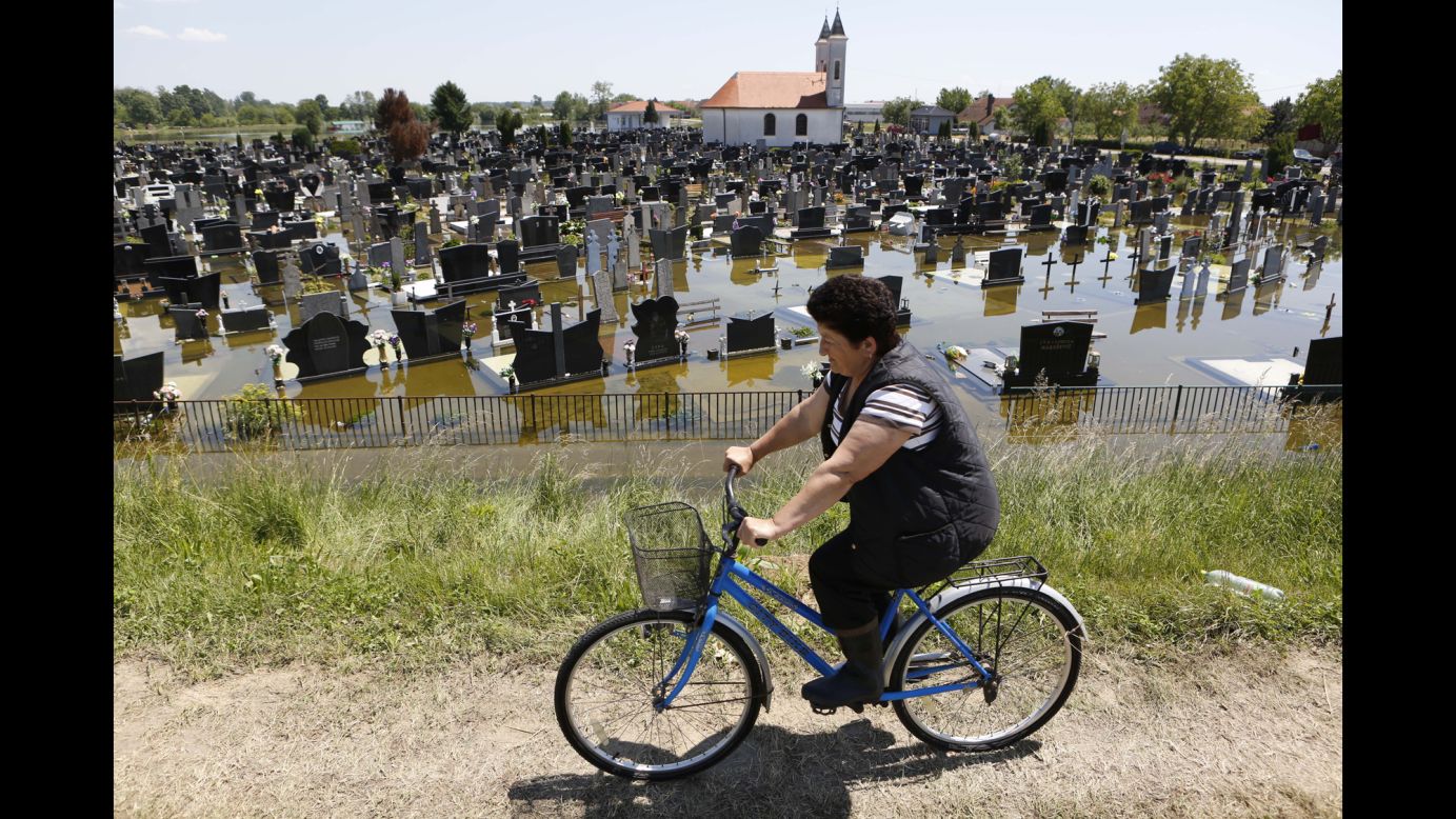 A woman rides a bicycle past a flooded cemetery in Domaljevac, Bosnia-Herzegovina, on Wednesday, May 21. 