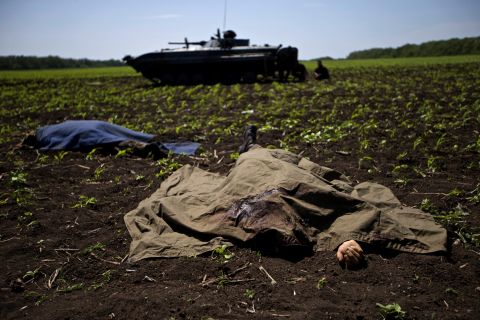 Bodies covered with blankets lie in a field near the village of Blahodatne, Ukraine, on May 22, as a Ukrainian soldier smokes next to his armored infantry vehicle.