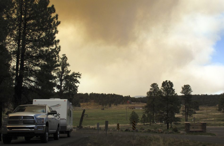 A vehicle heads out of Kachina Village as the wildfire sends plumes of smoke into the air on May 21.