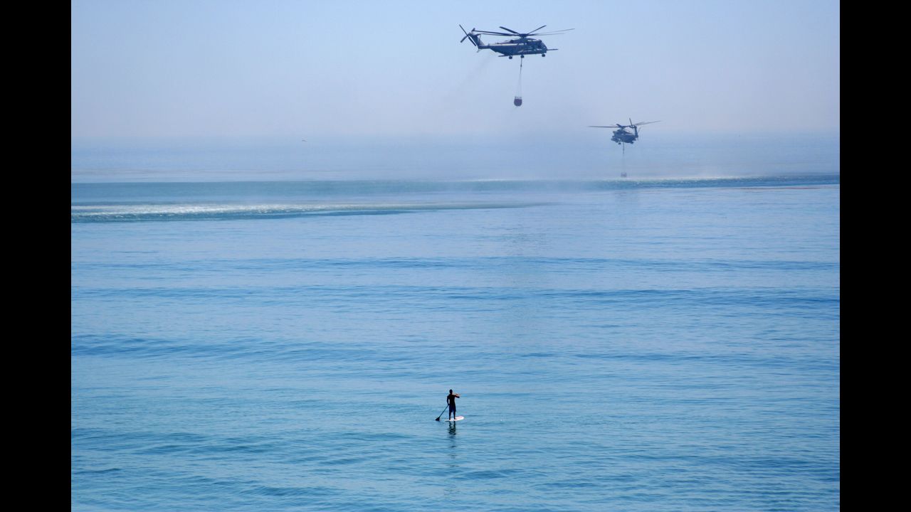 A paddleboarder watches two helicopters grab water from the Pacific Ocean to fight wildfires near Camp Pendleton, California, on May 16.