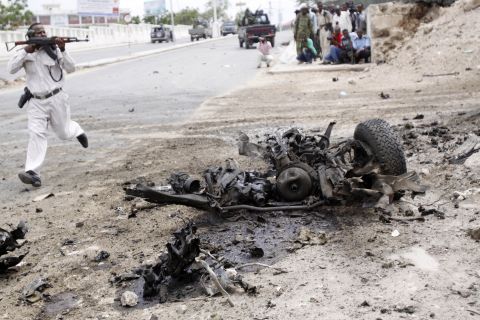 A Somali soldier runs to fight near the wreckage of a car bomb.