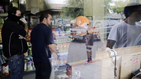 IV Deli Mart owner Michael Hassan, second from left, cleans up his store with employees May 24 as onlookers gather outside one of the shooting scenes. Student Christopher Martinez, 20, was getting a sandwich at the deli when he was fatally shot.