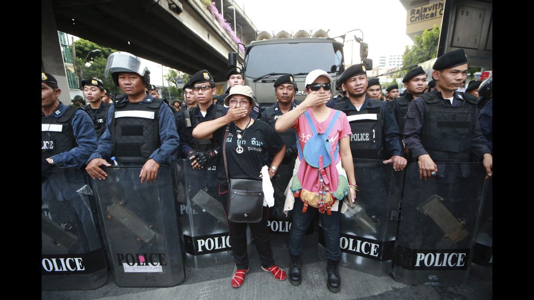 Two protesters stand in front riot police during an anti-coup demonstration in Bangkok on Monday, May 26. Demonstrators have taken to the streets in opposition to the coup, while some Thais express hope the military will bring an end to the political crisis.