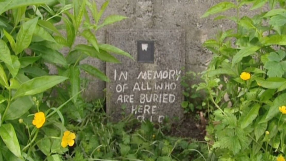 A marker to those buried at a former home for unwed mothers sits against a stone wall. 