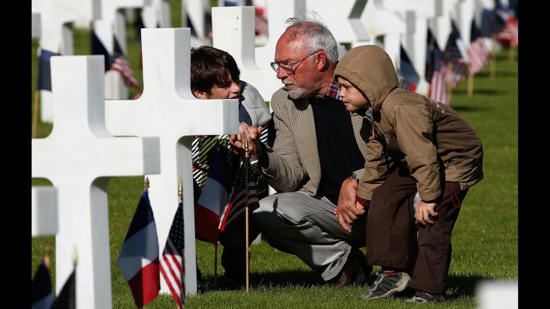 Michel Colas talks with his grandsons Samuel Colas and Rafael Schneider at the Normandy American Cemetery in Colleville-sur-Mer, France.