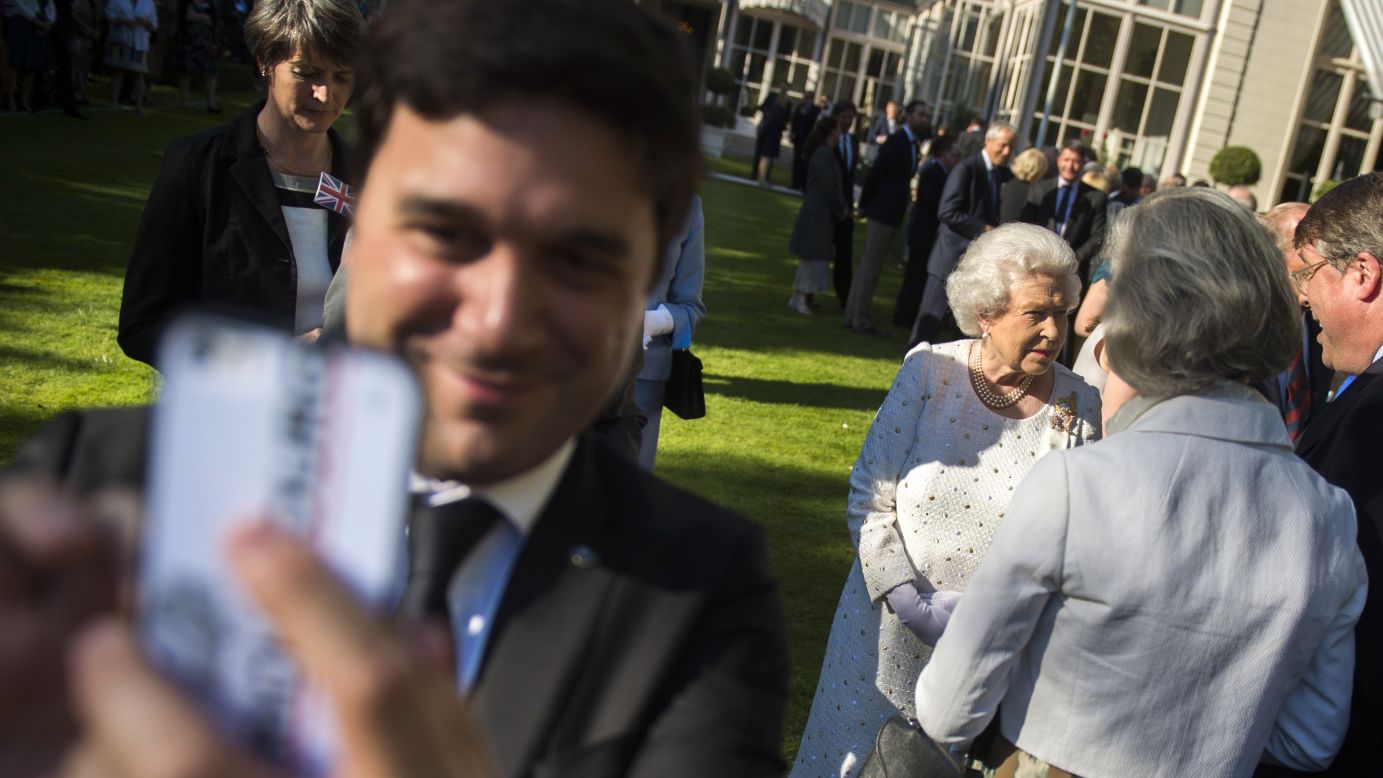 A man takes a selfie while, in the background, Queen Elizabeth II meets guests during a garden party at the British Embassy in Paris on Thursday, June 5.