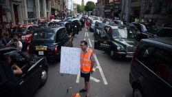 A demonstrator holds a placard as parked taxis block a street in central London during a protest by London black cab drivers against a new private taxi service 'Uber', a mobile phone app, on June 11, 2014. Taxi drivers brought parts of London, Paris and other European cities to a standstill on June 11 as they protested against new private cab apps such as Uber which have shaken up the industry. Thousands of London's iconic black cabs, many of them beeping their horns, filled the roads around Buckingham Palace, Trafalgar Square and the Houses of Parliament to the exclusion of any other vehicles. AFP PHOTO / CARL COURTCARL COURT/AFP/Getty Images