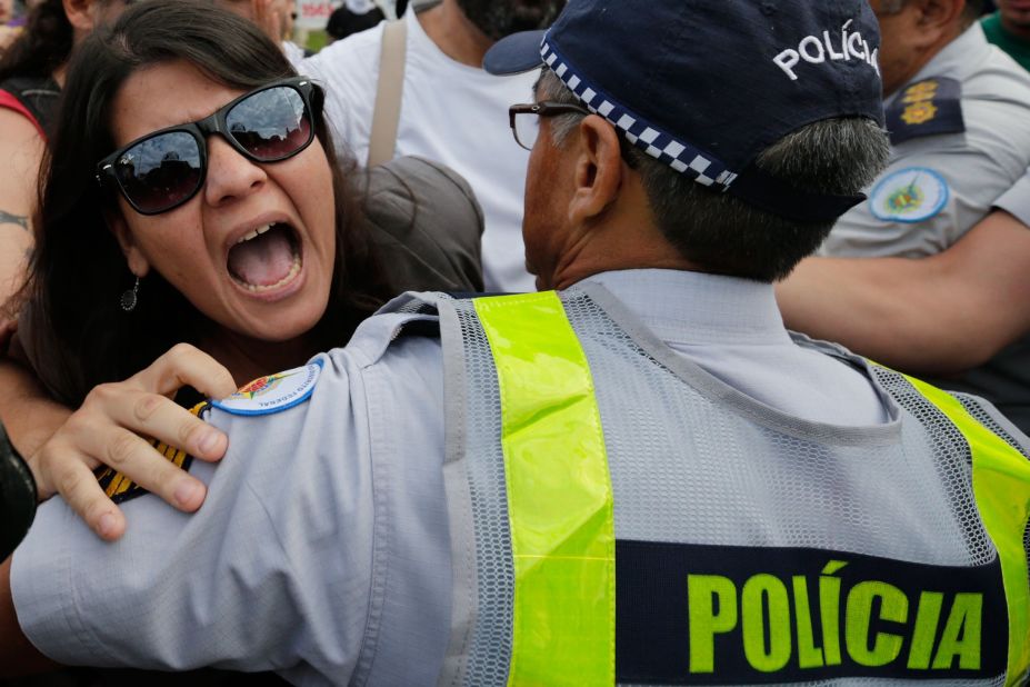 A demonstrator shouts as a military police officer pushes her back, trying to keep her and other protesters from entering the FIFA Fan Fest area.